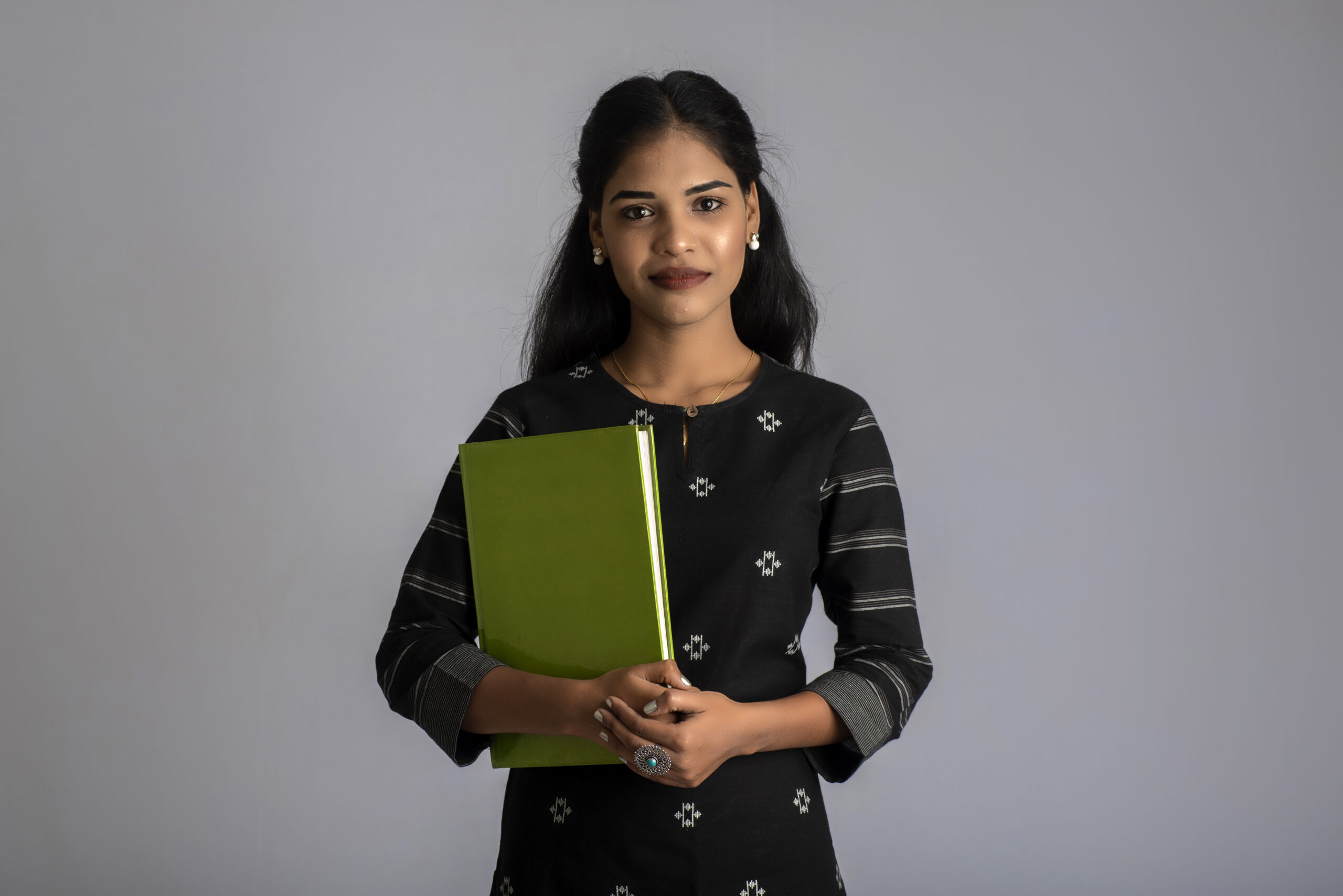 Pretty young girl holding book and posing on grey background